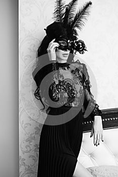 Glamorous brunette lady with a beautiful hairstyle and red lips, in an evening dress, a Venetian black mask with stylish accessori photo