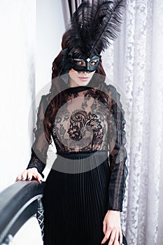 Glamorous brunette lady with a beautiful hairstyle and red lips, in an evening dress, a Venetian black mask with stylish accessori photo