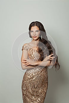 Glamorous brunette woman fashion model with make-up and long hair in golden evening gown against white studio background