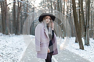 Glamorous cute young woman blonde in an elegant stylish hat in a knitted golf in a skirt in a fashionable pink coat posing