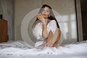 Glamorous girl sitting in a compact pose on white sheets.