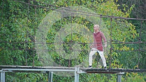 Glamorous handsome blond man sings standing on suspension bridge over river in beautiful pictorial place