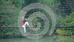 Glamorous handsome blond man sits on suspension bridge over river in beautiful pictorial place