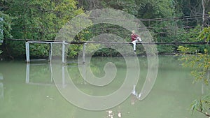 Glamorous handsome blond man sits on suspension bridge over river in beautiful pictorial place