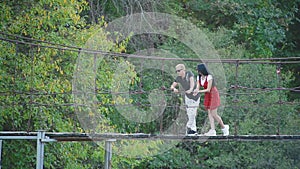 Glamorous handsome blond man and slim sexy young brunette woman stand and cute talk on suspension bridge