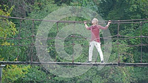 Glamorous handsome blond man stands on suspension bridge over river in beautiful pictorial place