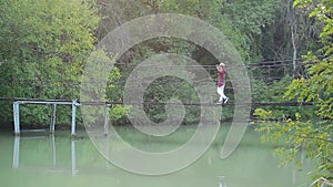 Glamorous handsome blond man walks on suspension bridge over river in amazing beautiful pictorial place