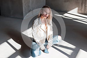 Glamorous modern attractive blond woman in vintage green cowboy boots in a summer leather jacket in ripped jeans sits in a room