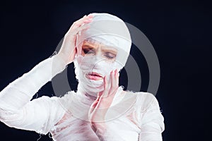 Glamorous mummy woman in bandages all over her body in studio black background. Halloween party or plastic surgery