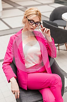 Glamorous pretty young professional woman in classic stylish pink suit with fashionable hairstyle straightens glasses while