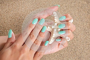 Glamorous Turquoise Manicure: Hands Holding Starfish on Beach Sand