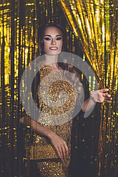 Glamorous woman celebrity with makeup wearing gold dress smiling on golden bokeh background