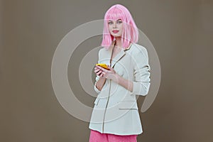 glamorous woman pink wig white jacket phone in hands gray background