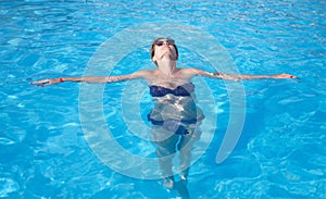 Glamorous woman in stylish sunglasses enjoys swimming in turquoise water in pool