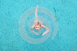 Glamorous woman in a swimming costume swims in a pool in blue water. View from above