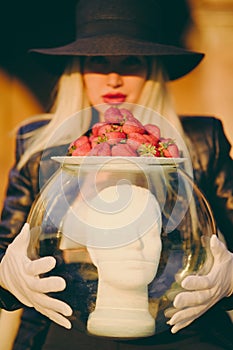 Glamorous woman in white gloves holding aquarium with mannequin man's head. Blurry focus face. Fashion concept.