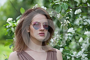 Glamorous young adult woman female model with clean fresh skin, make-up and brown hair in blossom garden on green leaves