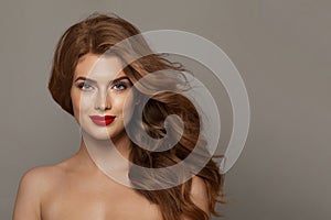 Glamorous young female model with healthy hair, makeup and shiny clear skin posing against gray studio wall background.