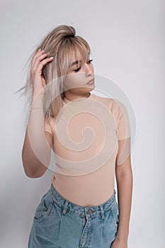 Glamorous young woman model in a stylish t-shirt in fashionable jeans stands near a vintage white wall in the room. Trendy girl in