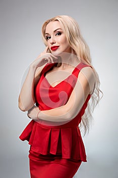 Glamorous young woman in red dress on gray background