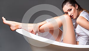 Glamorous young woman in tub. Studio shot of adorable curly female model in white dress. Fashion portrait of woman