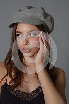 Glamorous young woman wears fashionable dress posing with fluttering hair at grey wall