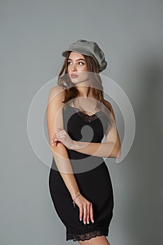 Glamorous young woman wears fashionable dress posing with fluttering hair at grey wall