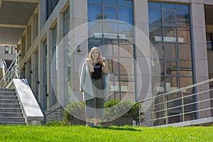 Glamorous young woman wears fashionable dress posing with fluttering hair at grey wall