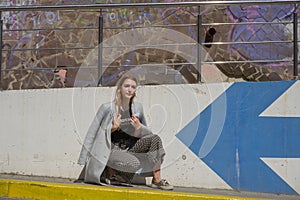 Glamorous young woman wears fashionable dress posing with fluttering hair at grey wall