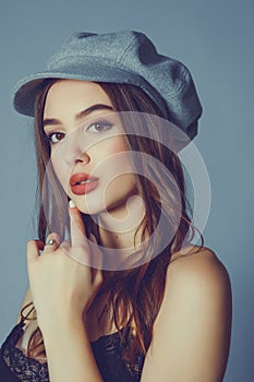 Glamorous young woman wears fashionable dress posing with fluttering hair at grey wall. Girl put forward hand