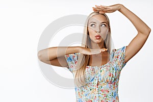 Glamour blond girl pucker lips, making hand box over her face, standing silly against white background