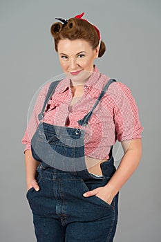 Glamour brunette female in american worker style with pin-up makeup. Woman in denim and red shirt in studio on gray