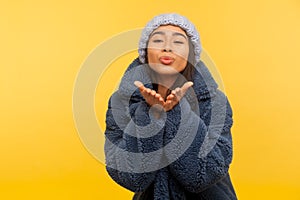 Glamour and fashion. Portrait of lovely carefree girl in warm winter hat and fur coat, stylish urban outfit, sending air kiss