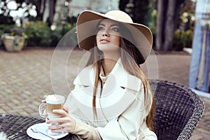 Glamour girl with dark straight hair wears luxurious beige coat with elegant hat,