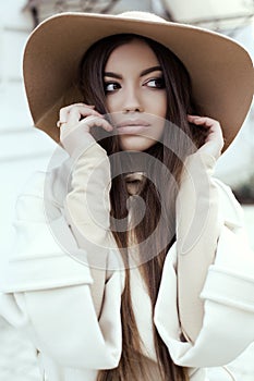 Glamour girl with dark straight hair wears luxurious beige coat with elegant hat