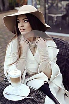 Glamour girl with dark straight hair wears luxurious beige coat with elegant hat