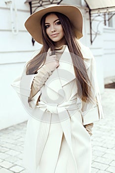 Glamour girl with dark straight hair wears luxurious beige coat with elegant hat,