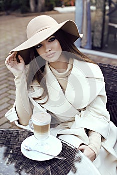 Glamour girl with dark straight hair wears luxurious beige coat with elegant hat,