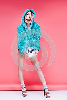 glamour girl posing in blue fur coat with disco ball on pink,