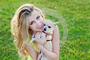 Glamour happy smiling girl or woman holding cute chihuahua puppy dog on green lawn on the sunset