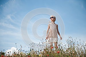 Glamour little girl in fashion summer dress and sunglasses standing on the background of blue cloudy sky