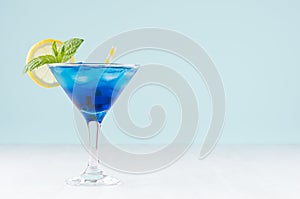 Glamour tropical fruit blue cocktail with curacao, ice cubes, lemon slice, yellow straw, mint in misted martini glass.