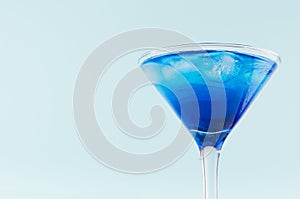 Glamour tropical fruit blue cocktail with curacao, ice cubes in misted martini glass in modern mint color background, top part.