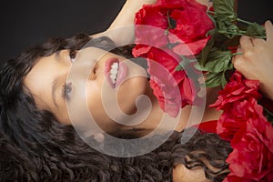 Glamourous studio portrait of young Latina woman holding red flowers