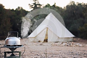 Glamping lifestyle. Boiling kettle with steam near big retro camping tent. Luxury travel accomodation into the forest