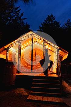 Glamping from tent houses in the forest in the dark. silhouette of a woman