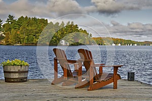 Retirement Living - Two Muskoka chairs sitting on a boat dock facing a calm lake with trees and cottages in the background photo