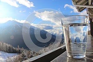 Glas of mineral water on railing with mountain landscape and blue cloudy sky