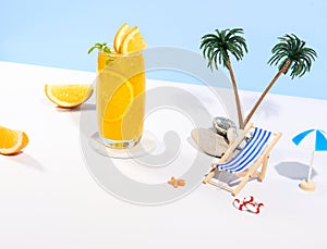 Glass of 100% Orange juice with orange slices fruits on sea beach with white sand. Summer sea vacation and travel concept.