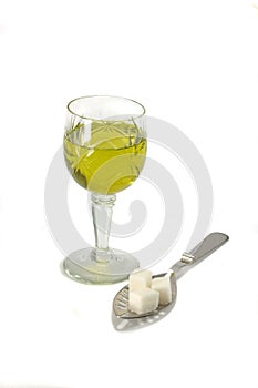 Glass with absinth and spoon with sugar pieces